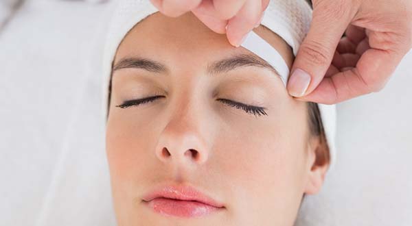 cosmetologist removing wax during a facial for the eyebrows